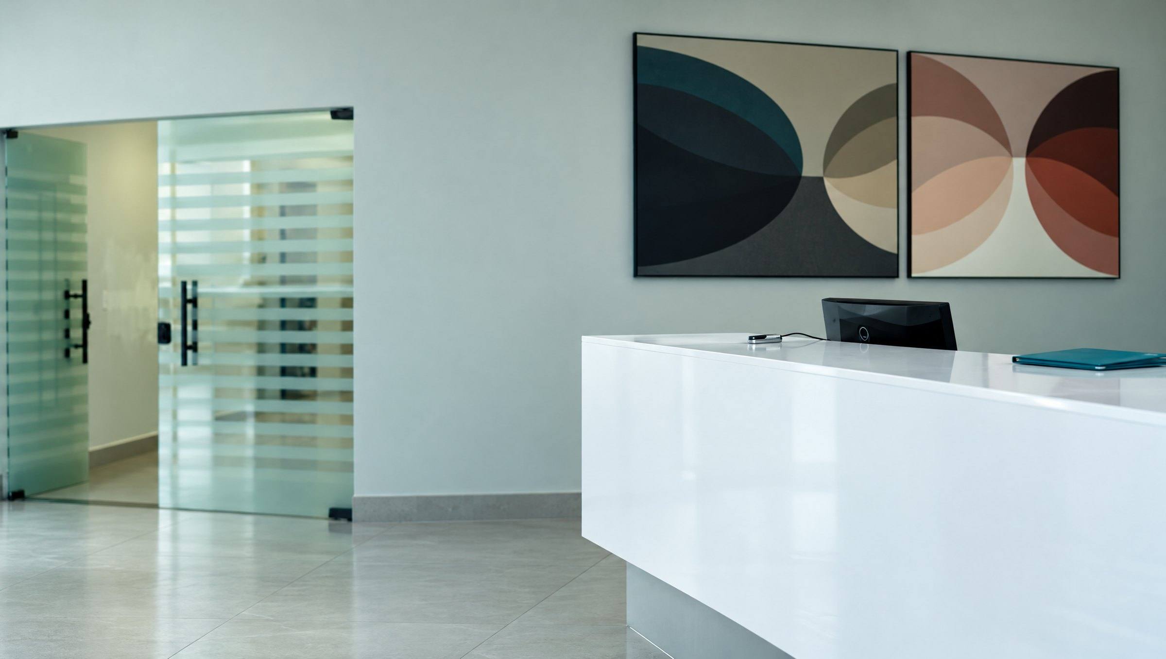 Recepção da ECOS: o balcão branco com uma pasta teal, portas de vidro listradas e dois quadros com círculos ao fundo.